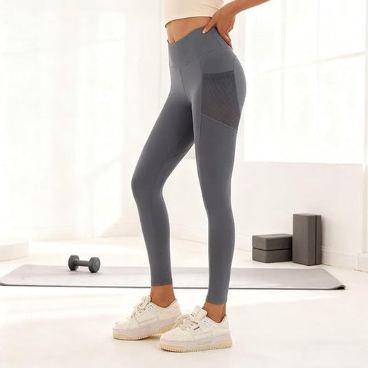 Person wearing gray leggings with a white background wih yoga mat and weight with blocks in background