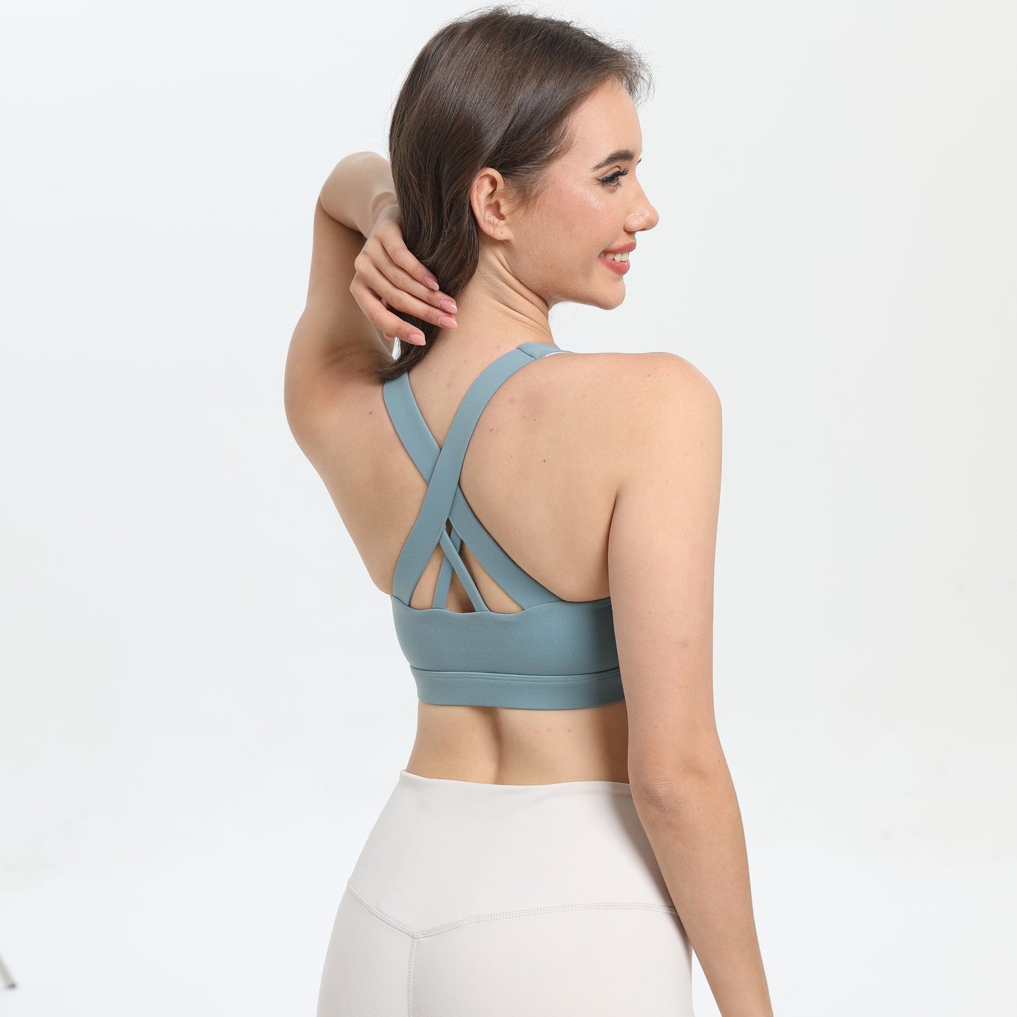 Woman wearing a blue sports bra and white leggings on a light gray background