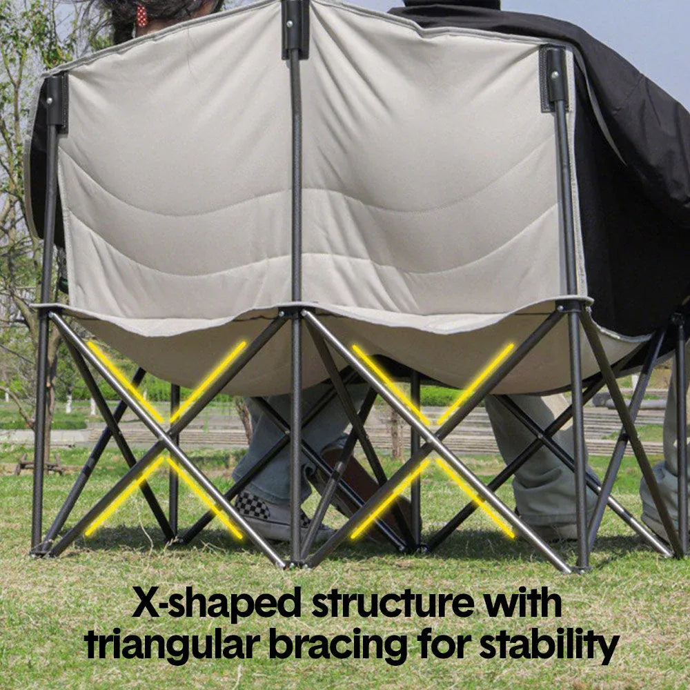 Camping chair with X-shaped structure and triangular bracing for stability on grass.
