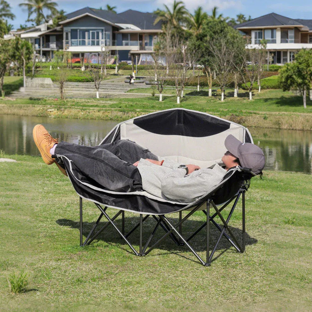 Person lying on a hexagonal outdoor chair by a pond with houses in the background